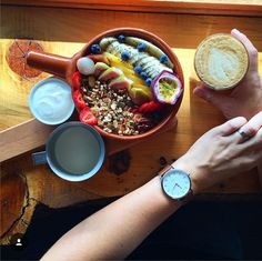 a person holding a cup of coffee and a bowl of food with fruit on it