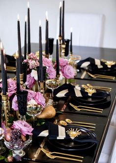 a long table with black and gold place settings, flowers and candles on top of it