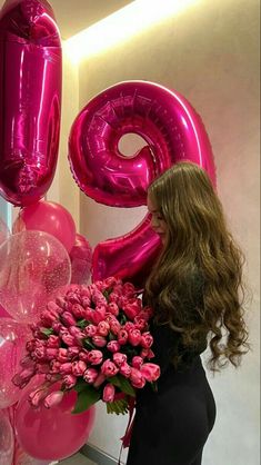 a woman standing in front of pink balloons and flowers with the number twenty nine on it