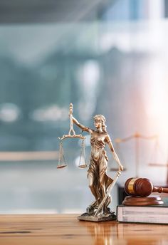 a lady justice statue next to a gaven and book on a wooden table in front of a blurry background