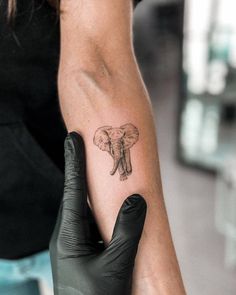 an elephant tattoo on the arm of a woman's left hand, with black gloves