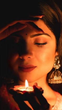 a woman holding a lit candle in her hand and looking at it with eyes closed