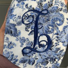 a person holding up a blue and white fabric monogrammed to the letter f