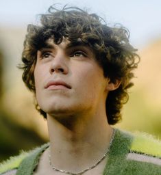 a young man with curly hair wearing a green sweater looking up at something in the distance