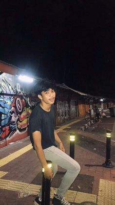 a young man standing on top of a pole next to a wall covered in graffiti