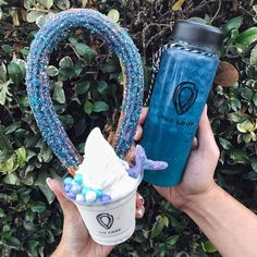 a person holding up a blue drink in their left hand and a plastic cup with candy on it