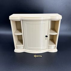 a white cabinet with two shelves and a key on the bottom one shelf has an open door