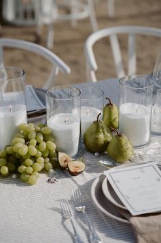 a table topped with glasses filled with white wine next to pears and other fruit