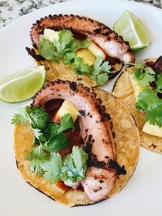 three tacos on a plate with limes and cilantro