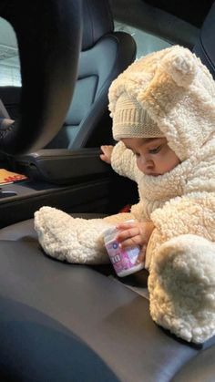 a baby sitting in the back seat of a car wearing a teddy bear costume and holding a bottle