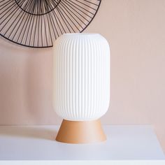 a white vase sitting on top of a table next to a wall decoration with a fan behind it