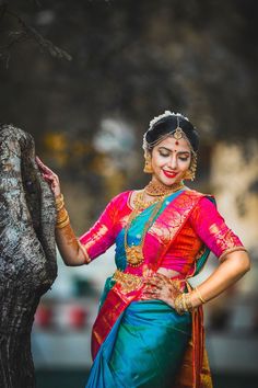 a woman in a colorful sari standing next to a tree