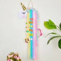 a wall hanging with a unicorn horn and pom poms on it next to a potted plant