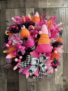 a wreath made out of pink and orange items on a wooden wall with black and white bows