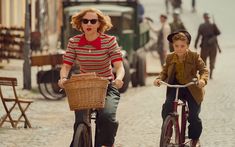 a woman riding a bike next to a boy on a street with people walking around