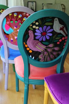 four colorful chairs with birds and flowers painted on the back one chair has a purple cushion