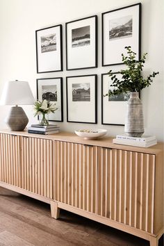 a wooden sideboard with pictures on the wall above it and a lamp next to it