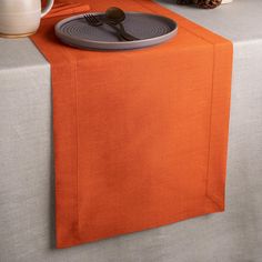 an orange table runner with a fork and knife on it next to a white vase