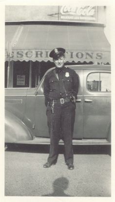 an old black and white photo of a police officer standing in front of a car