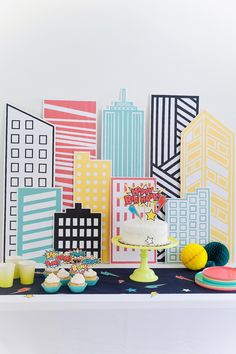 a table topped with cakes and cupcakes next to tall buildings in the background