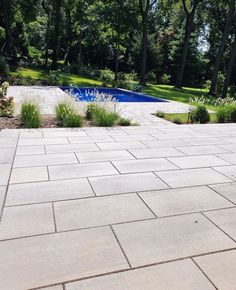 an empty patio next to a swimming pool in the middle of some trees and bushes