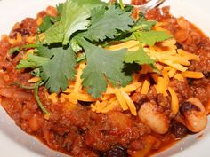 a white plate topped with chili and meat covered in cheese, cilantro and parsley