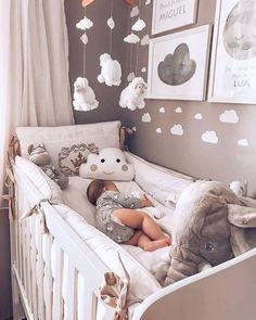 a baby laying in a crib with stuffed animals hanging from the ceiling and pictures on the wall