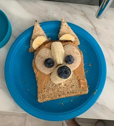 a piece of bread with peanut butter, banana and blueberries in the shape of a dog's face