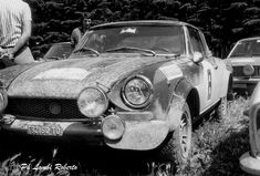 an old race car is parked in the grass with two men standing next to it