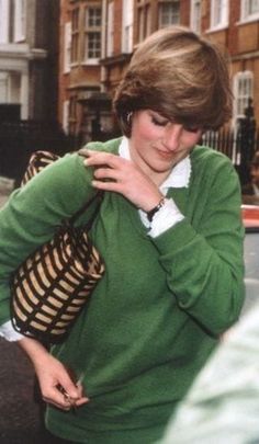 a woman in a green sweater is walking down the street with her hand on her shoulder