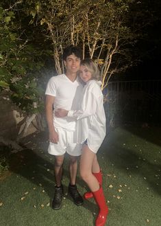 a man and woman dressed up in white posing for a photo outside at night with their arms around each other