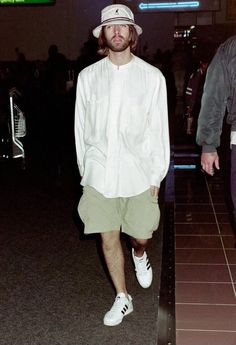 a man in white shirt and green shorts walking through an airport with his hat on