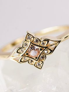 a close up view of a gold ring with an orange stone in the center and diamonds around it