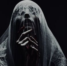 a ghostly woman covering her face with white veil and holding hands up to her mouth