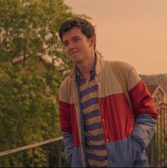 a young man is standing on a balcony with trees in the background and houses behind him