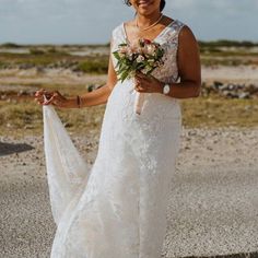 a woman in a white wedding dress holding a flower bouquet and smiling at the camera