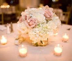 a vase filled with white and pink flowers on top of a table covered in candles