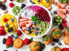 a white bowl filled with fruit next to muffins and other fruits on a table