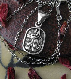 Material: 100% Sterling silver Weight: 2.7 grams Size: More than 3/8 inch wide x 1/2 inch tall excluding bail (10 x 14mm) Item number: wh055 Like most ancient Egyptian art, Anubis is depicted here with head in profile, but eye and shoulders shown frontally. His image is set within a frame resembling the oval cartouches of Egyptian hieroglyphs. Anubis' profile is in relief, raised against its background, with details effectively accented with oxidation. Anubis, who is most often shown in the form Silver Ankh Necklace For Ceremonial Use, Silver Ankh Necklace For Ceremonial Occasions, Silver Symbolic Rectangular Jewelry, Ancient Silver Pendant Necklace, Ancient Style Silver Necklace For Gift, Ancient Silver Collectible Jewelry, Ancient Style Collectible Silver Jewelry, Ancient Style Silver Jewelry Gift, Silver Ancient Style Jewelry For Gift