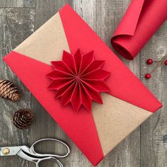 a red paper flower sitting on top of a piece of brown paper next to scissors