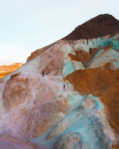 two people standing on top of a mountain covered in blue and brown colored rock formations