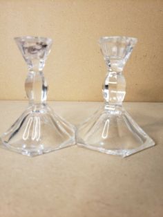 two clear glass candlesticks sitting side by side on a white surface with a tan wall in the background