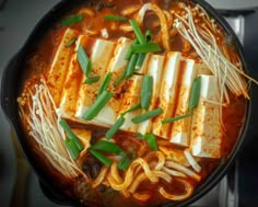 tofu, noodles and green onions are in a skillet on the stove top