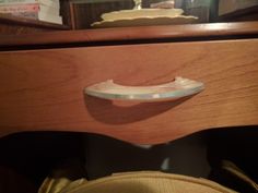 a close up of a drawer with a wooden handle on the bottom and an object in the background