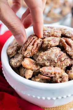 a hand picking up some pecans in a white bowl