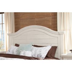 a bed with white headboard and pillows in front of a wooden paneled wall