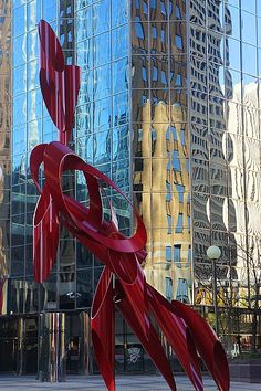 a large red sculpture in front of a tall glass building with skyscrapers behind it