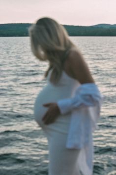 a pregnant woman standing on the edge of a body of water with her hands in her stomach