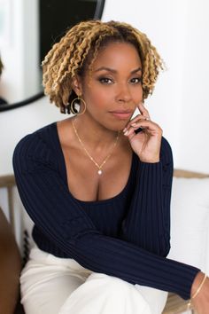 a woman sitting in a chair with her hand on her chin and looking at the camera