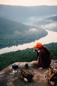 a woman sitting on top of a cliff next to a river